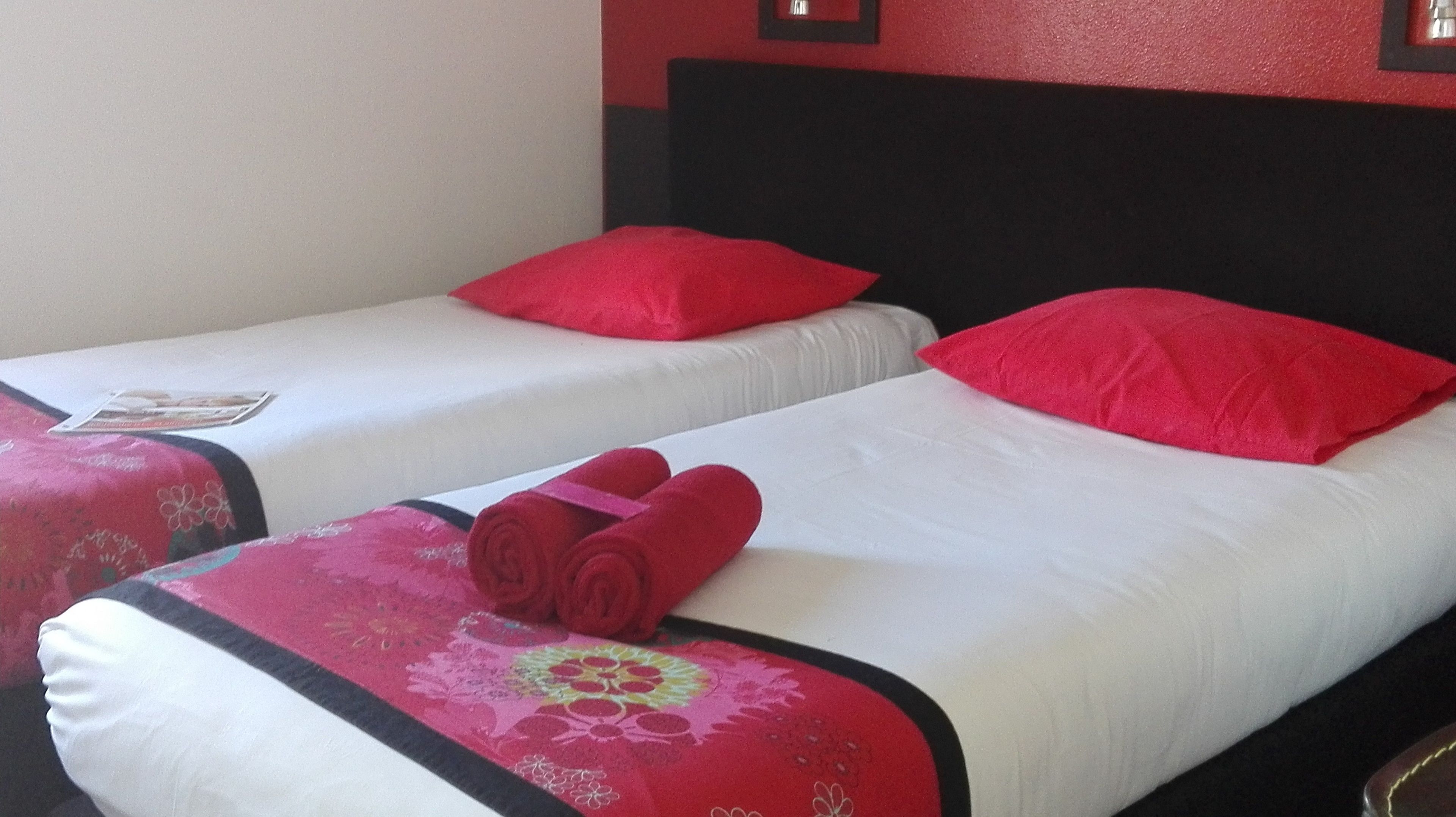 Two single beds with red pillows and a red towel on the bed.