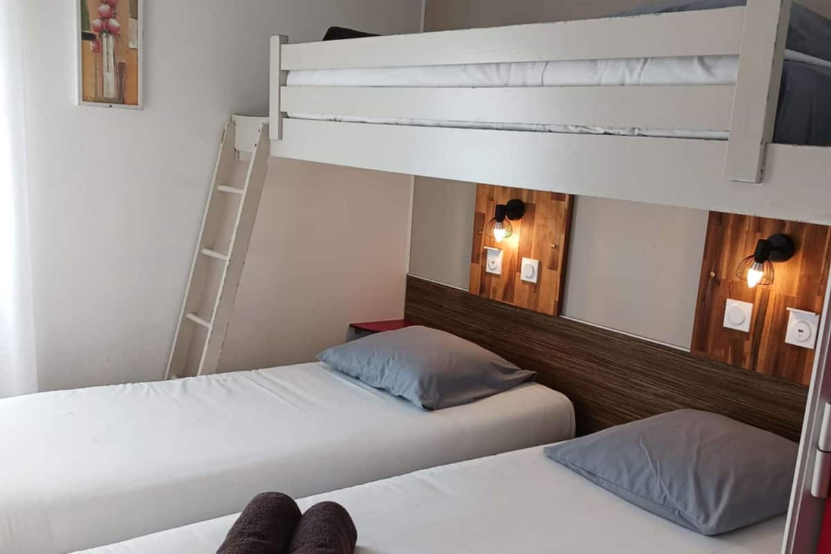 Habitación tipo dormitorio con dos camas individuales, una litera encima, una escalera y luces fijadas a la pared.