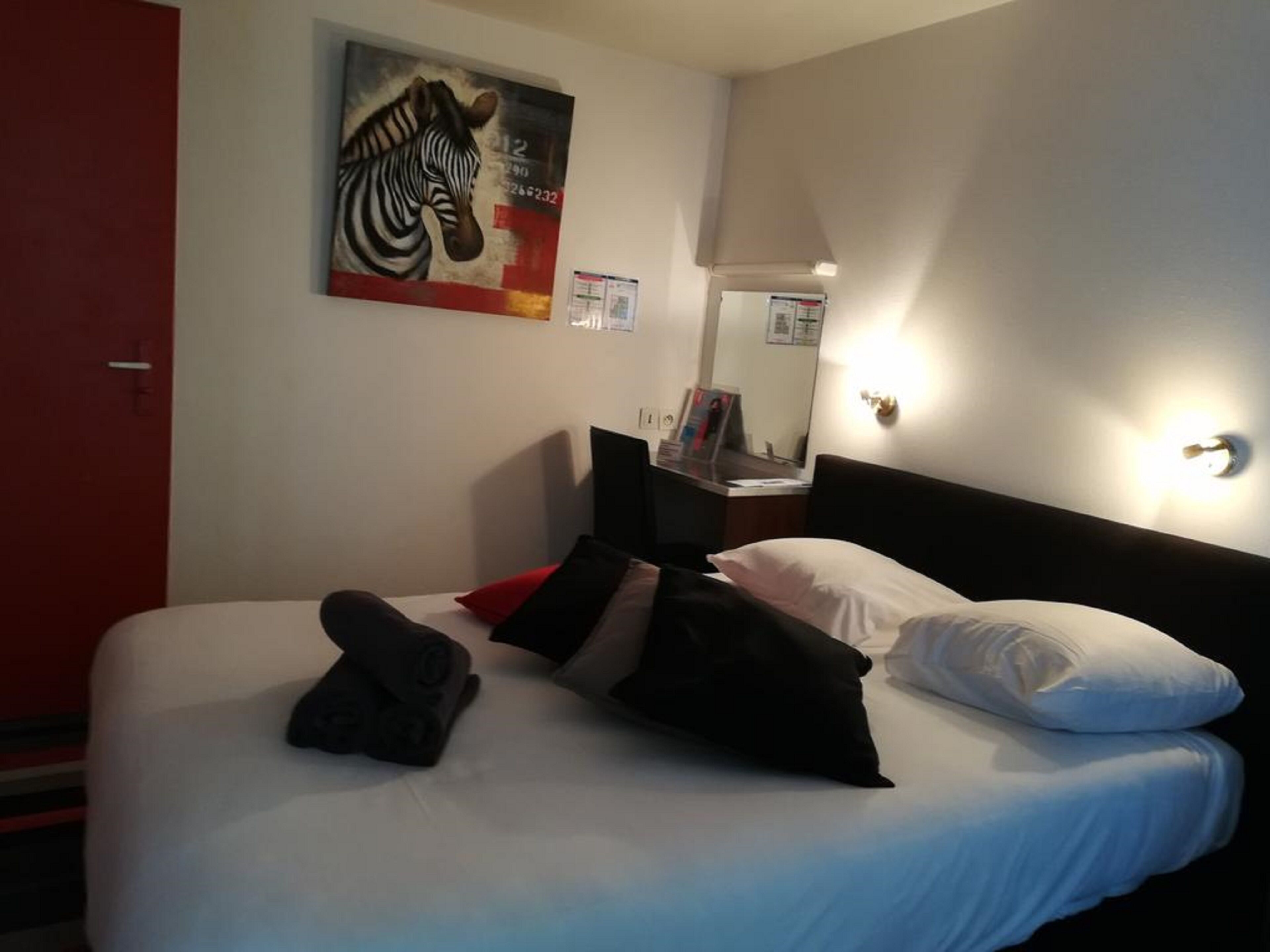 Habitación de hotel con cama, almohadas, una puerta roja, un cuadro de cebra, un espejo y una mesita de noche.
