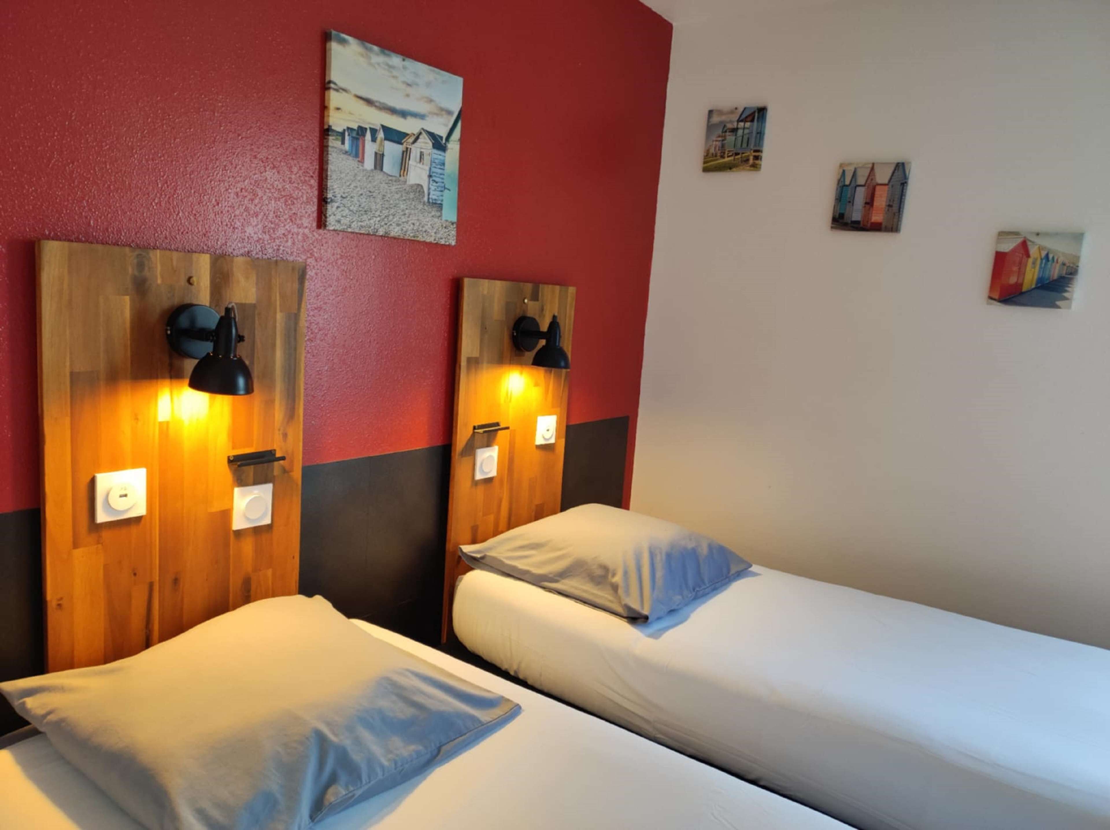 Une chambre d’hôtel avec deux lits, des têtes de lit en bois, des lampes fixées au mur et un mur d’accent de couleur rouge.