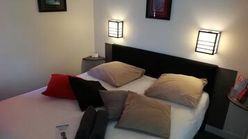 A neatly made bed with multiple pillows and a blanket, two bedside tables with lamps, and framed pictures on the walls.