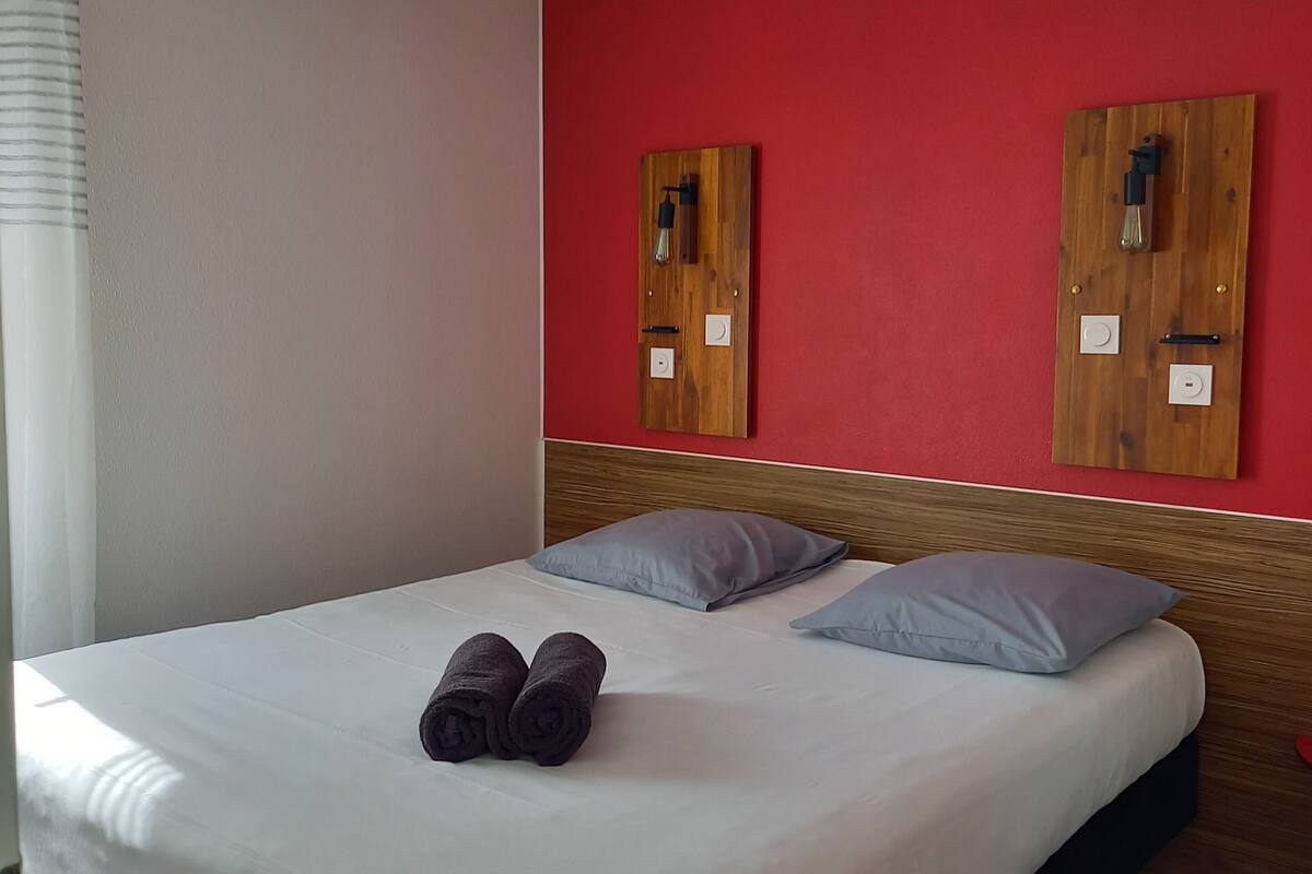 Habitación de hotel con una cama, dos almohadas, un cabecero de madera y una pared roja.