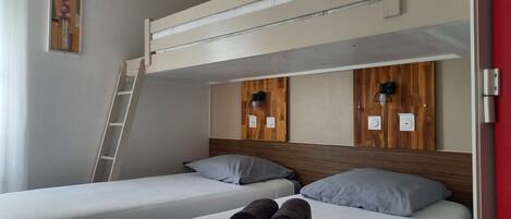 Habitación de hotel con dos camas individuales, una litera encima, cabeceros de madera, una escalera y un cuadro en la pared.