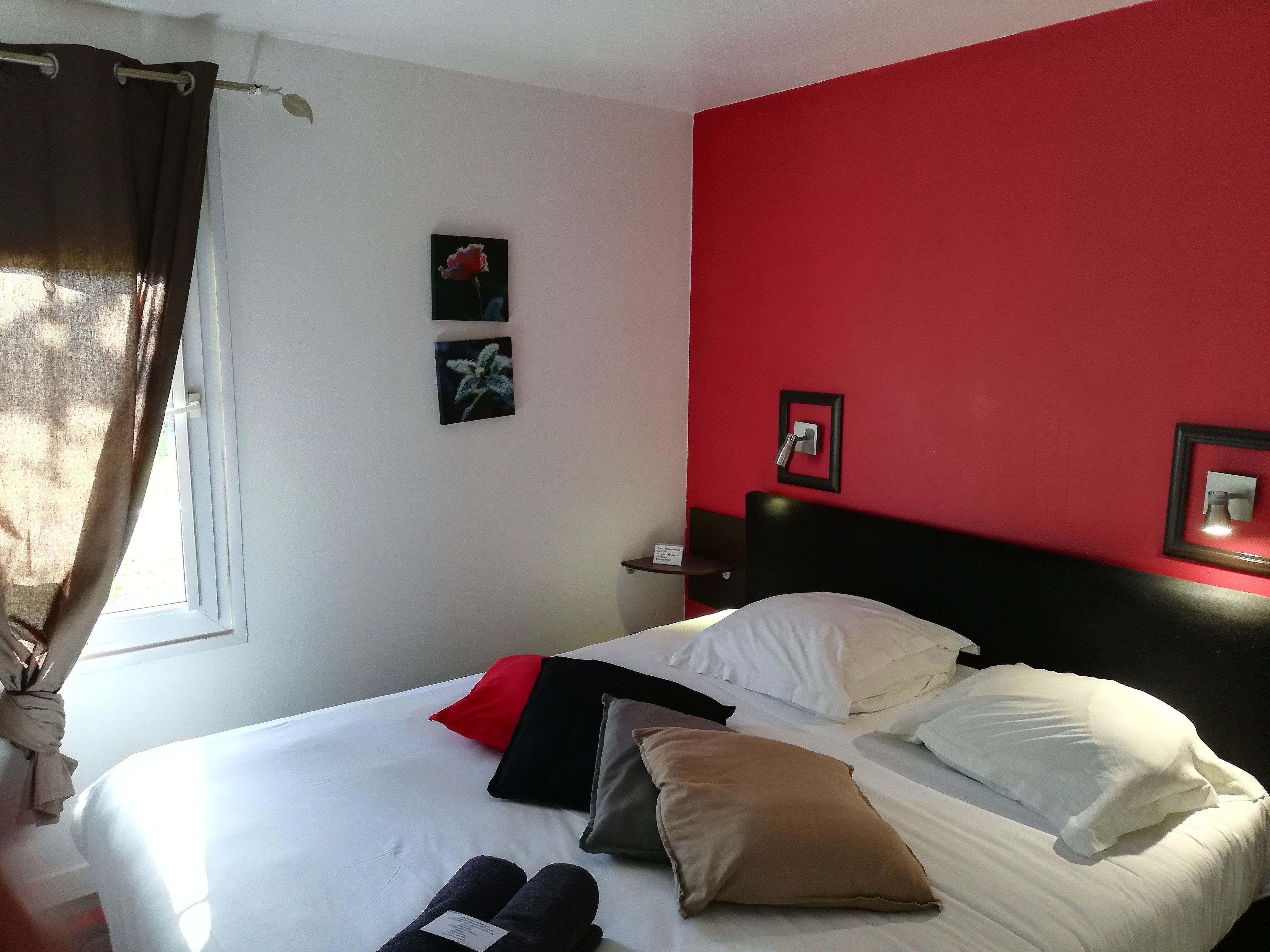 A hotel room with a bed, pillows, a nightstand, and a window with curtains.