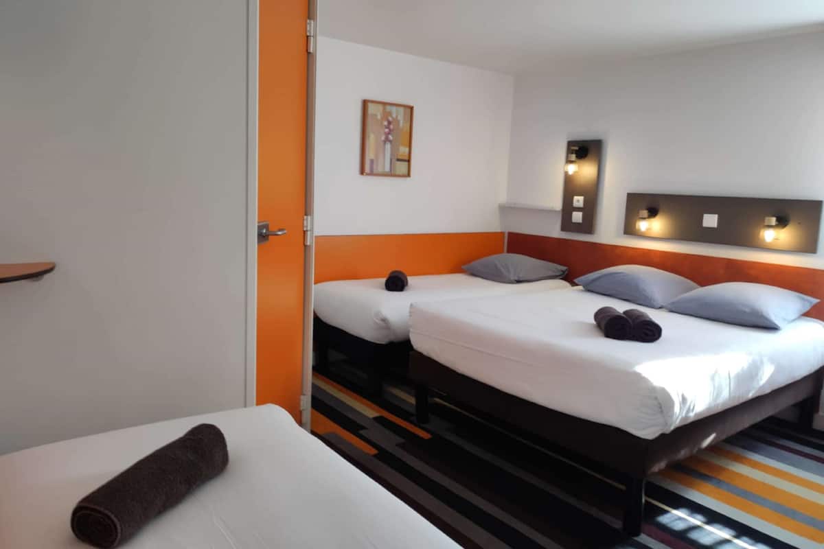 Una habitación de hotel con dos camas, un tapete a rayas, un cuadro en la pared y una puerta con marco naranja.