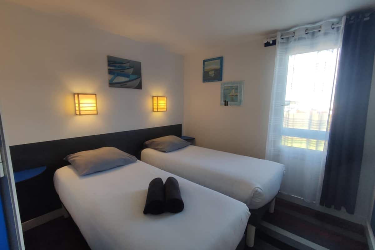 Habitación de hotel con dos camas, una ventana con cortinas, luces fijadas a la pared y obras de arte.