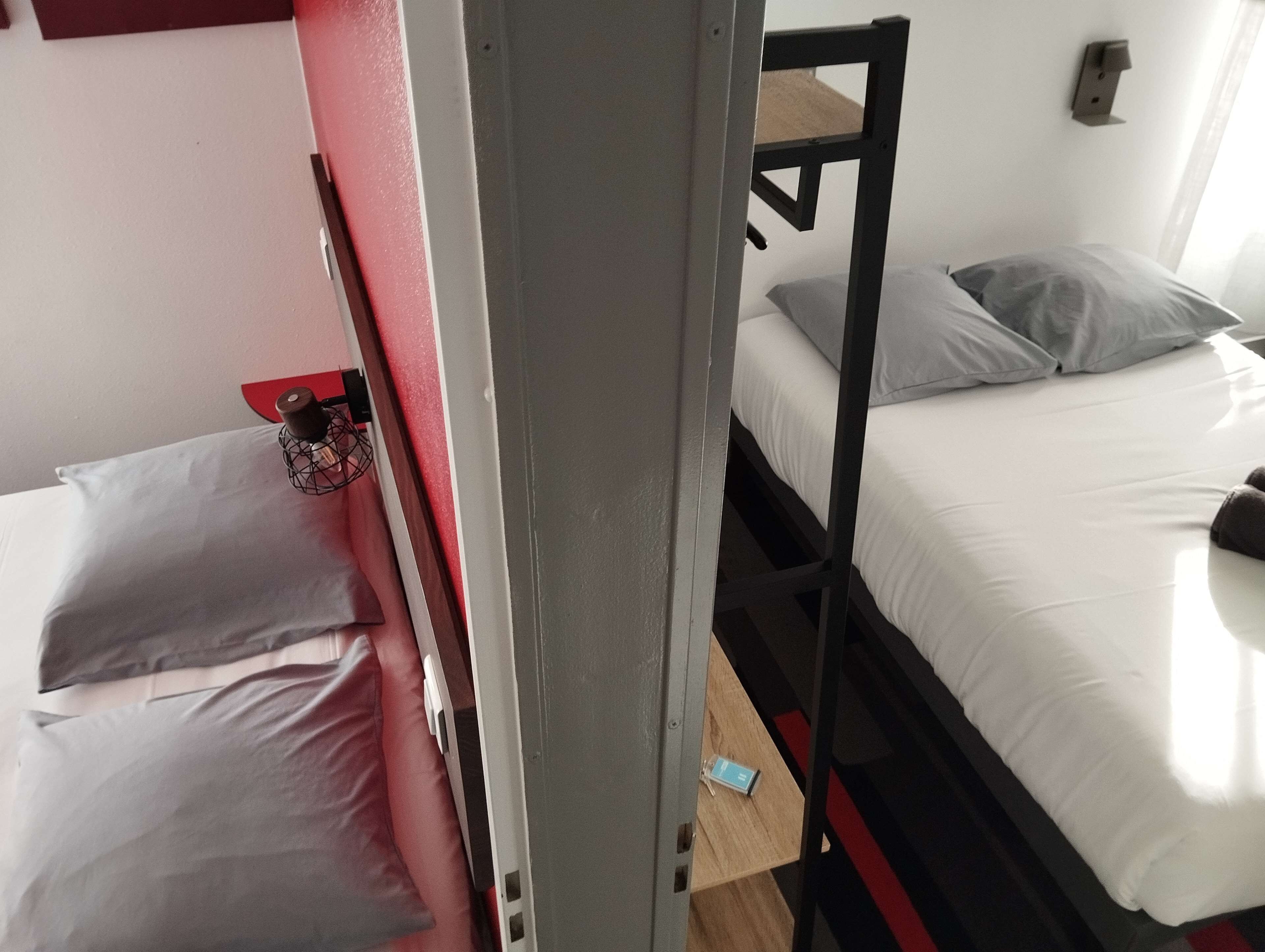 A bunk bed with a red frame, a white mattress, and a grey pillow.
