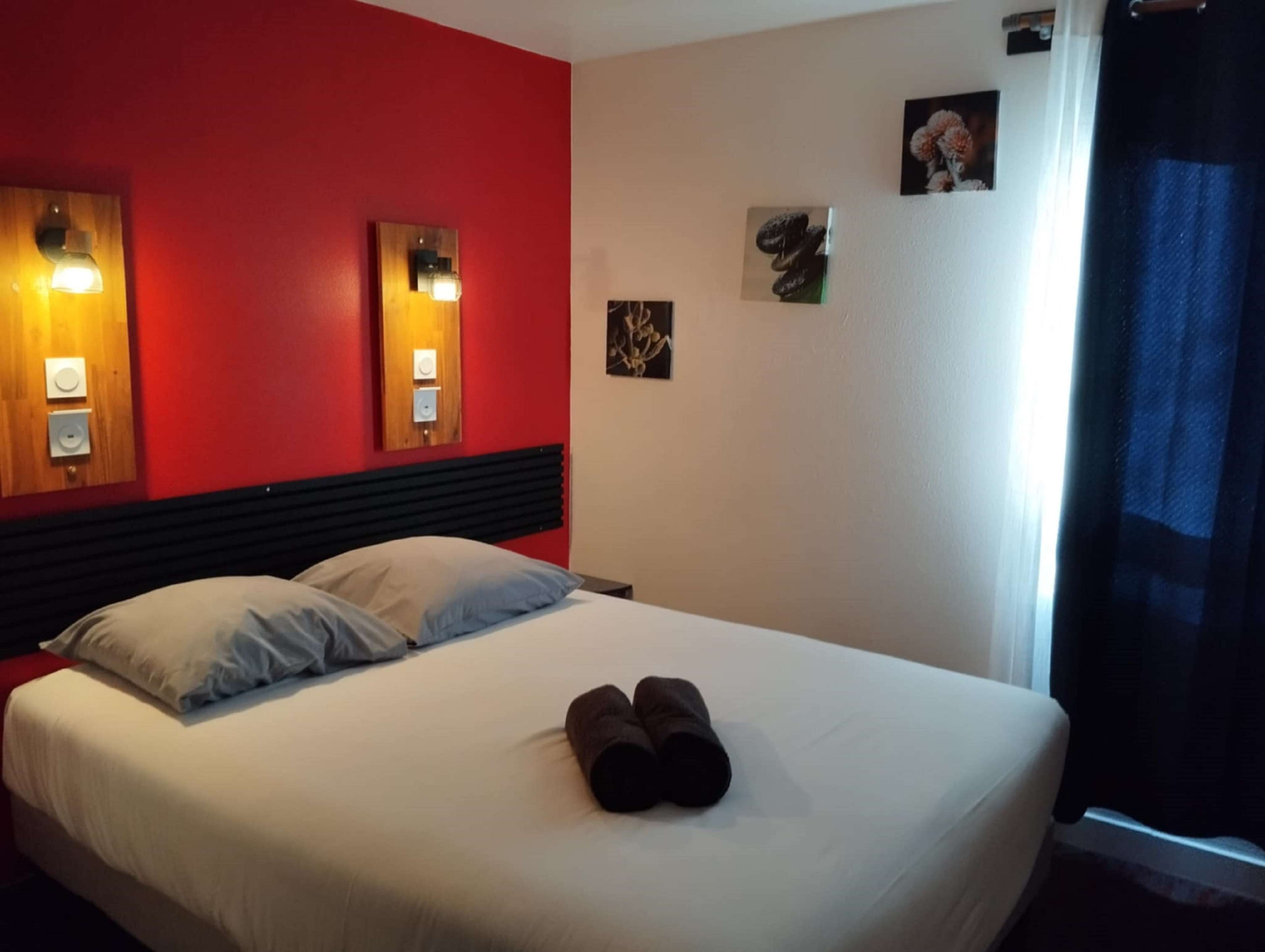 Habitación de hotel con una pared de acento roja, una cama con ropa de cama blanca y dos lámparas fijadas a la pared.