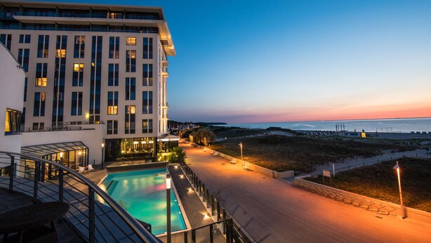 Ein modernes Hotel mit Pool, Blick auf den Strand und einem gut beleuchteten Weg.