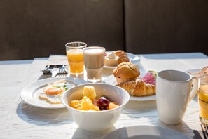 A breakfast setting with a plate of toast, a bowl of fruit, a muffin, and a cup of coffee on a table.
