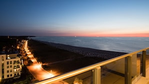 Eine Küstenstadt im Abendlicht mit einer langen Promenade, die zum Strand führt, modernen Gebäuden und freiem Blick auf das Meer.
