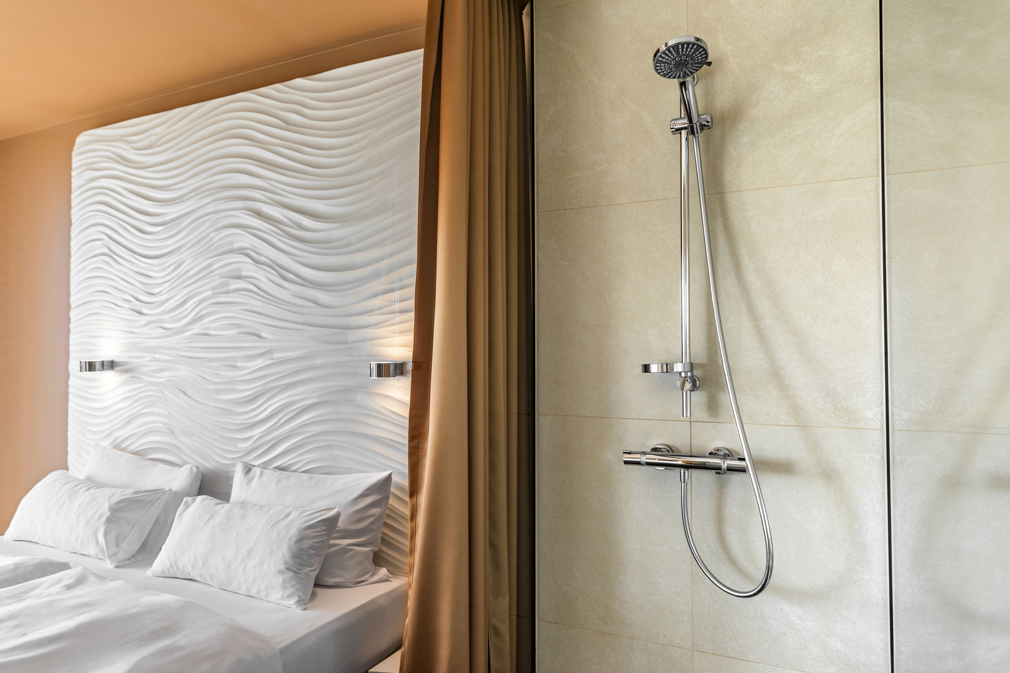 Een moderne badkamer met een douche, een bed met witte lakens en een gestructureerde wand.