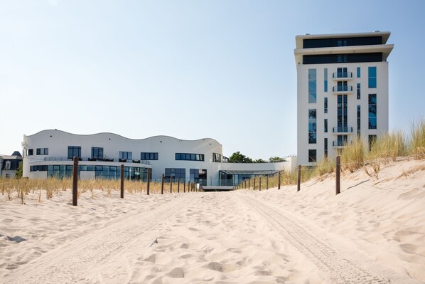 A modern building with a flat roof and large windows, surrounded by sand dunes.