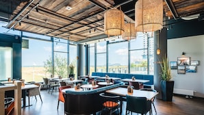 Ein modernes Restaurant mit hoher Decke, großen Fenstern und verschiedenen Sitzgelegenheiten, darunter Boxen und Tische.
