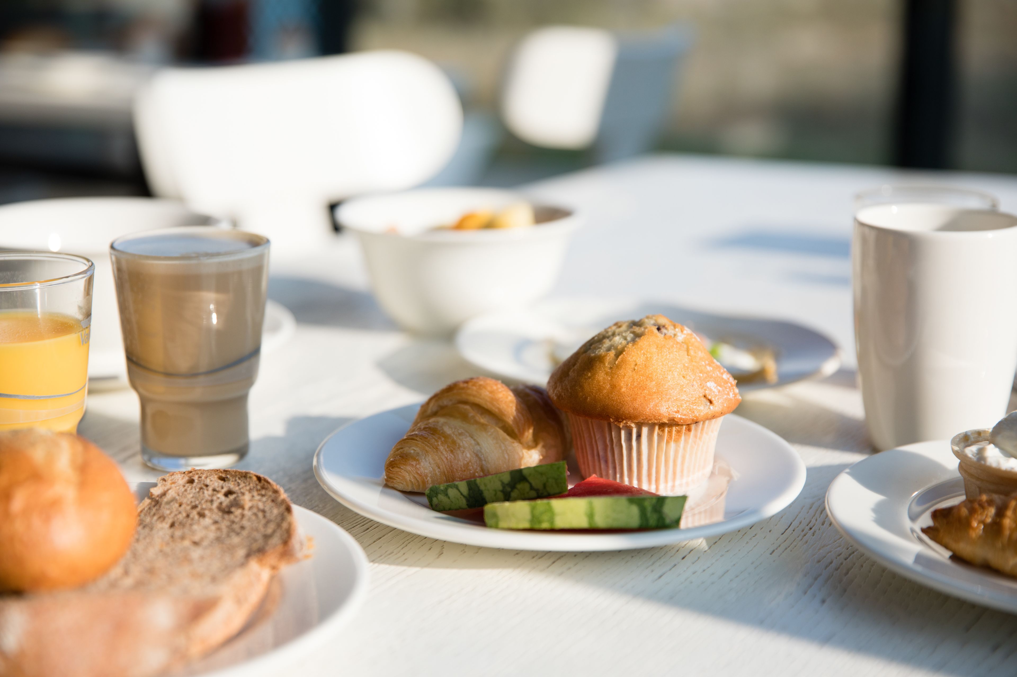 A breakfast table with croissants, muffins, and a glass of orange juice.