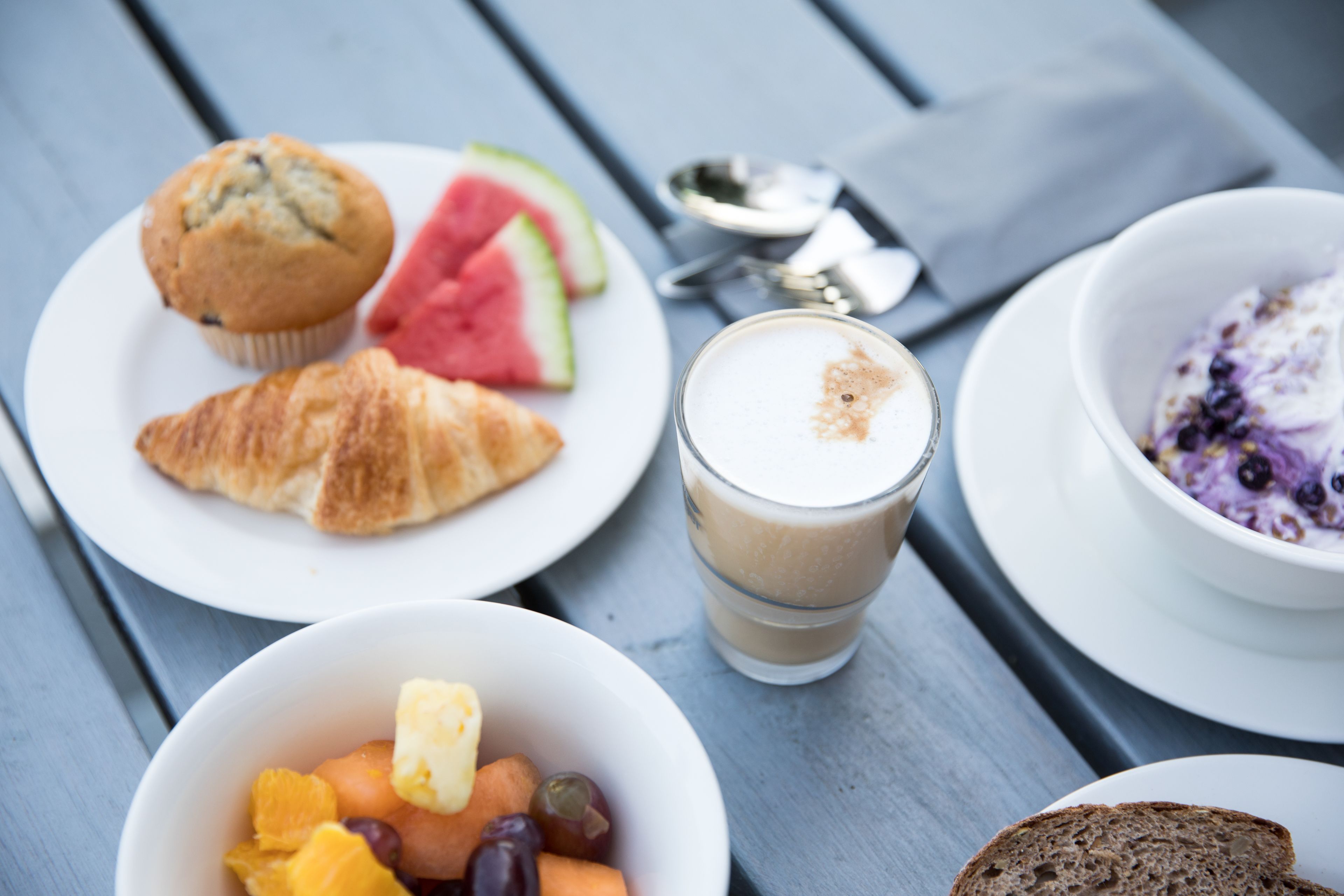 A table with food items including a croissant, muffin, watermelon, and a bowl of yogurt with berries.