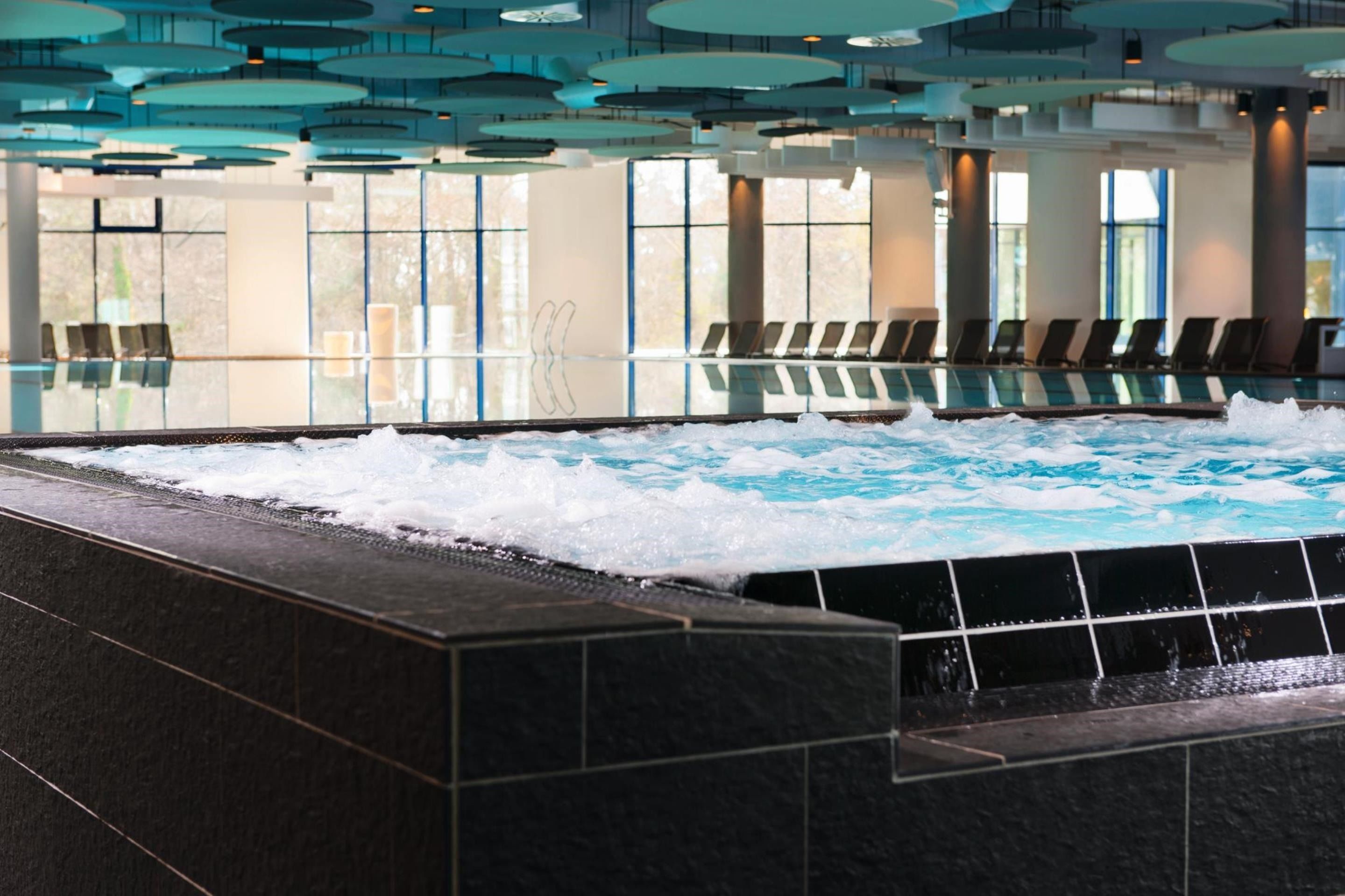 Una piscina interior moderna con efecto olas, zona de estar y ventanas amplias.