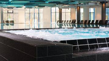 Ein moderner, überdachter Pool mit Wellenfunktion, Sitzgelegenheiten und großen Fenstern.