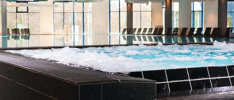 Una piscina interior moderna con efecto olas, zona de estar y ventanas amplias.