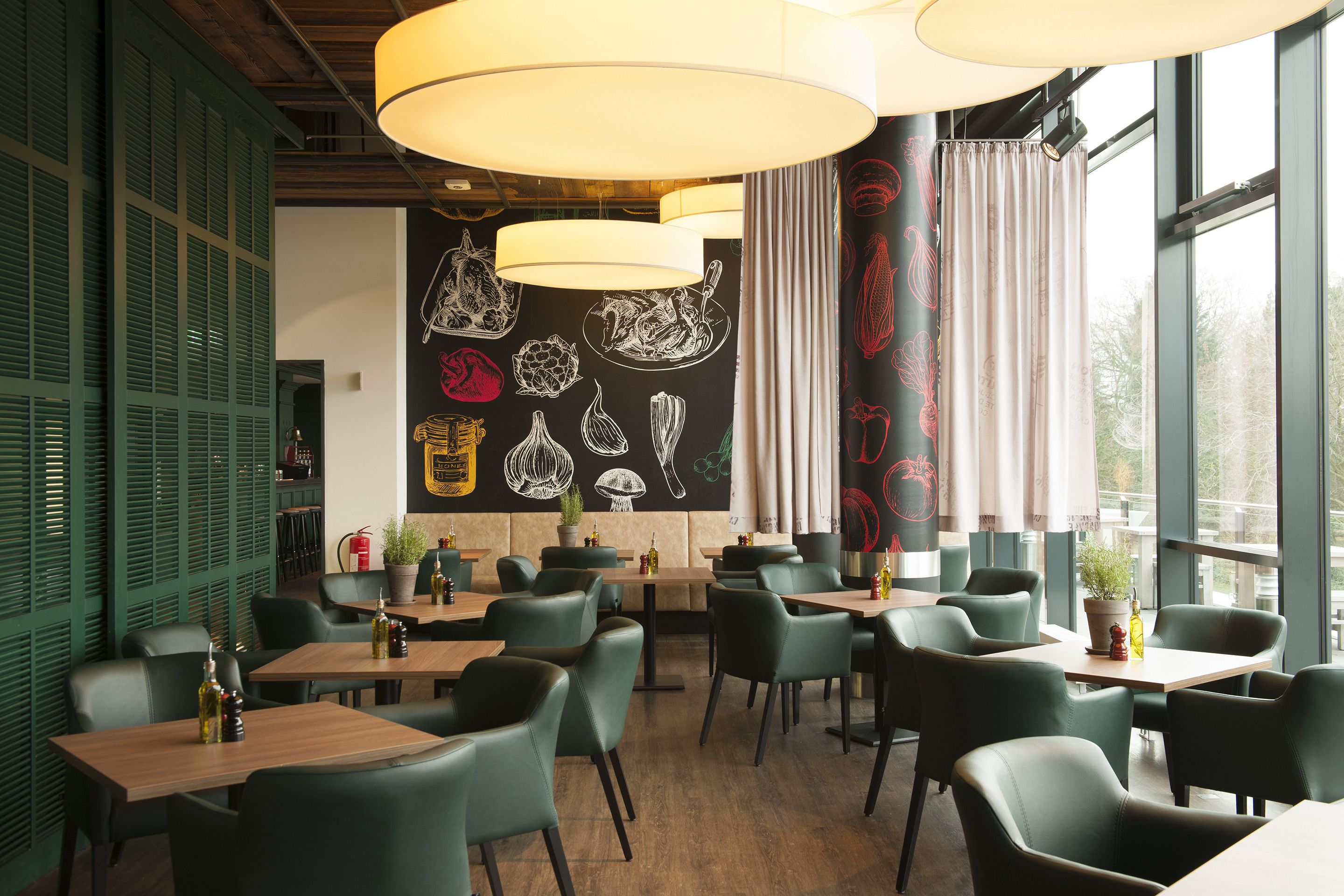 Een restaurantinterieur met groene stoelen, houten tafels en een zwarte wand met witte illustraties van eten.