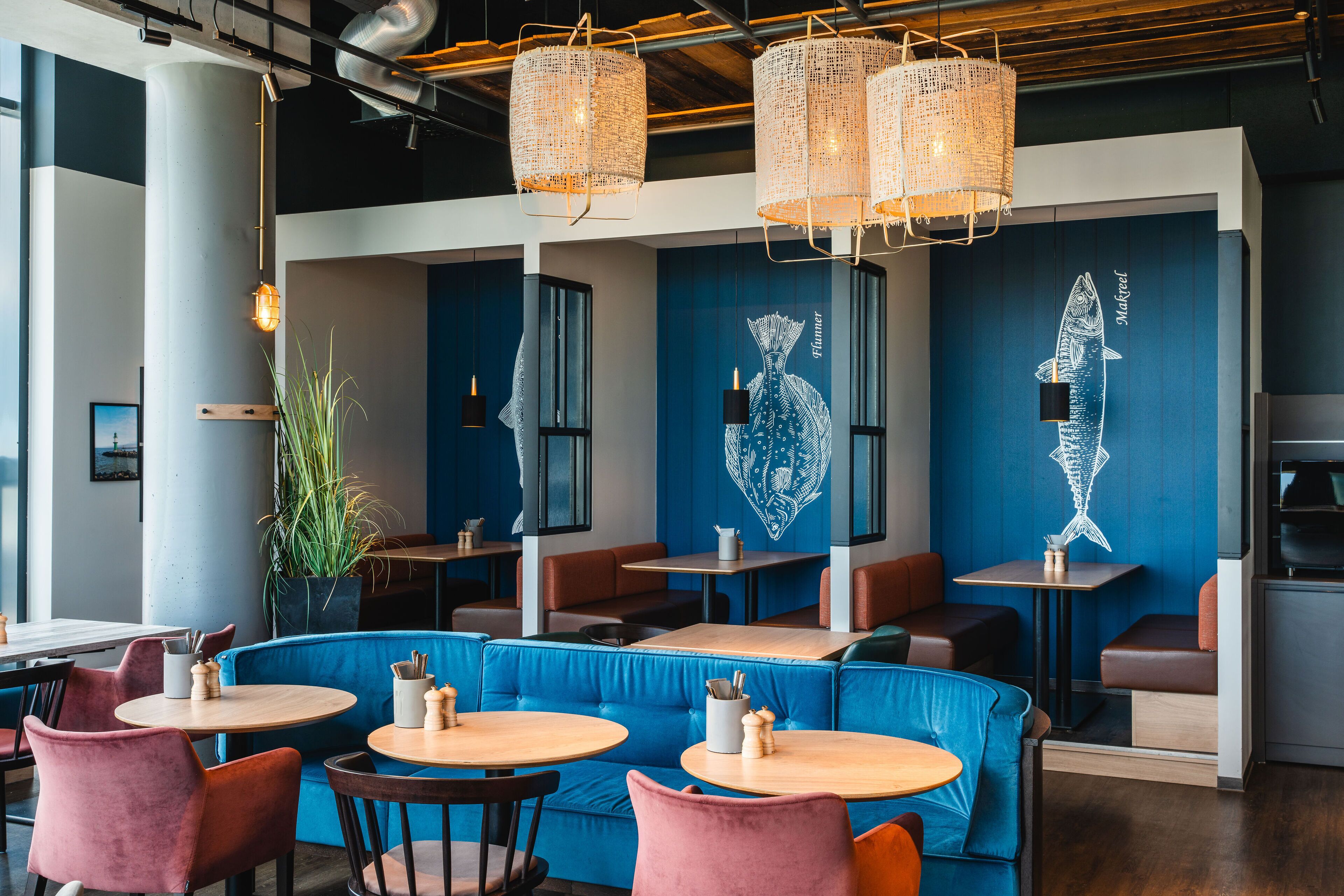 L’intérieur d’un restaurant avec des banquettes bleues, des tables en bois et des lampes en osier suspendues au plafond.