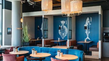L’intérieur d’un restaurant avec des banquettes bleues, des tables en bois et des lampes en osier suspendues au plafond.