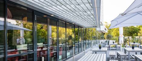 An outdoor patio with tables and chairs, large windows, and a modern architectural design.