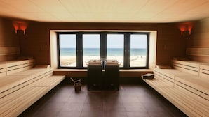Ein Saunaraum mit Holzbänken und einem großen Fenster mit Blick auf den Strand.