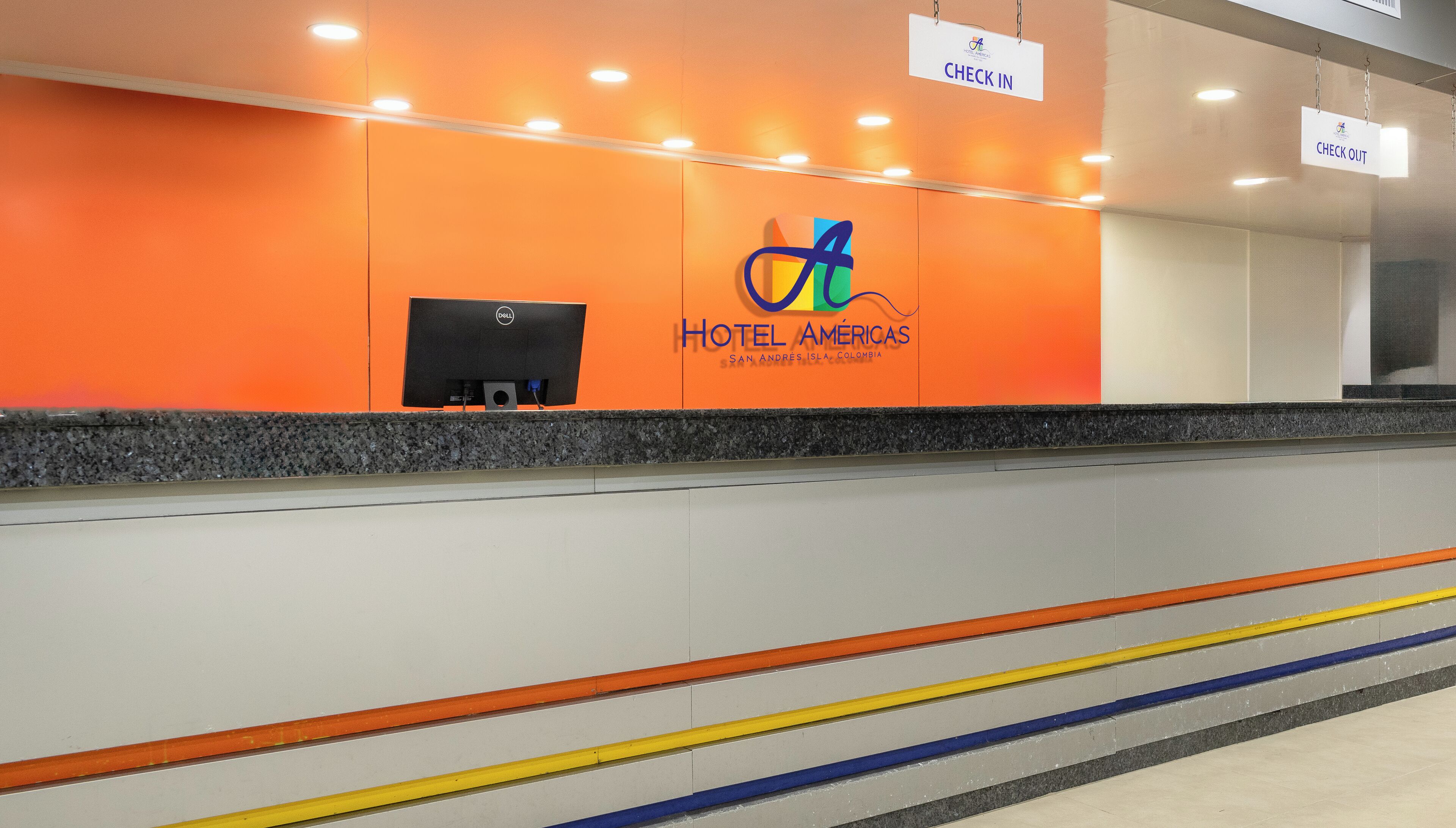 A check-in area with an orange wall, a Dell computer, and a sign indicating check-in and check-out areas.