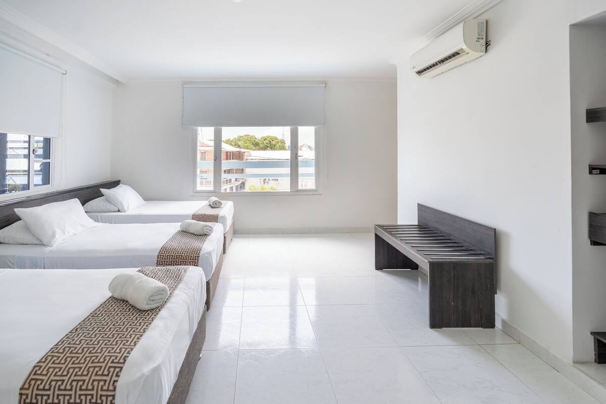 A hotel room with two beds, a bench, and a large window.