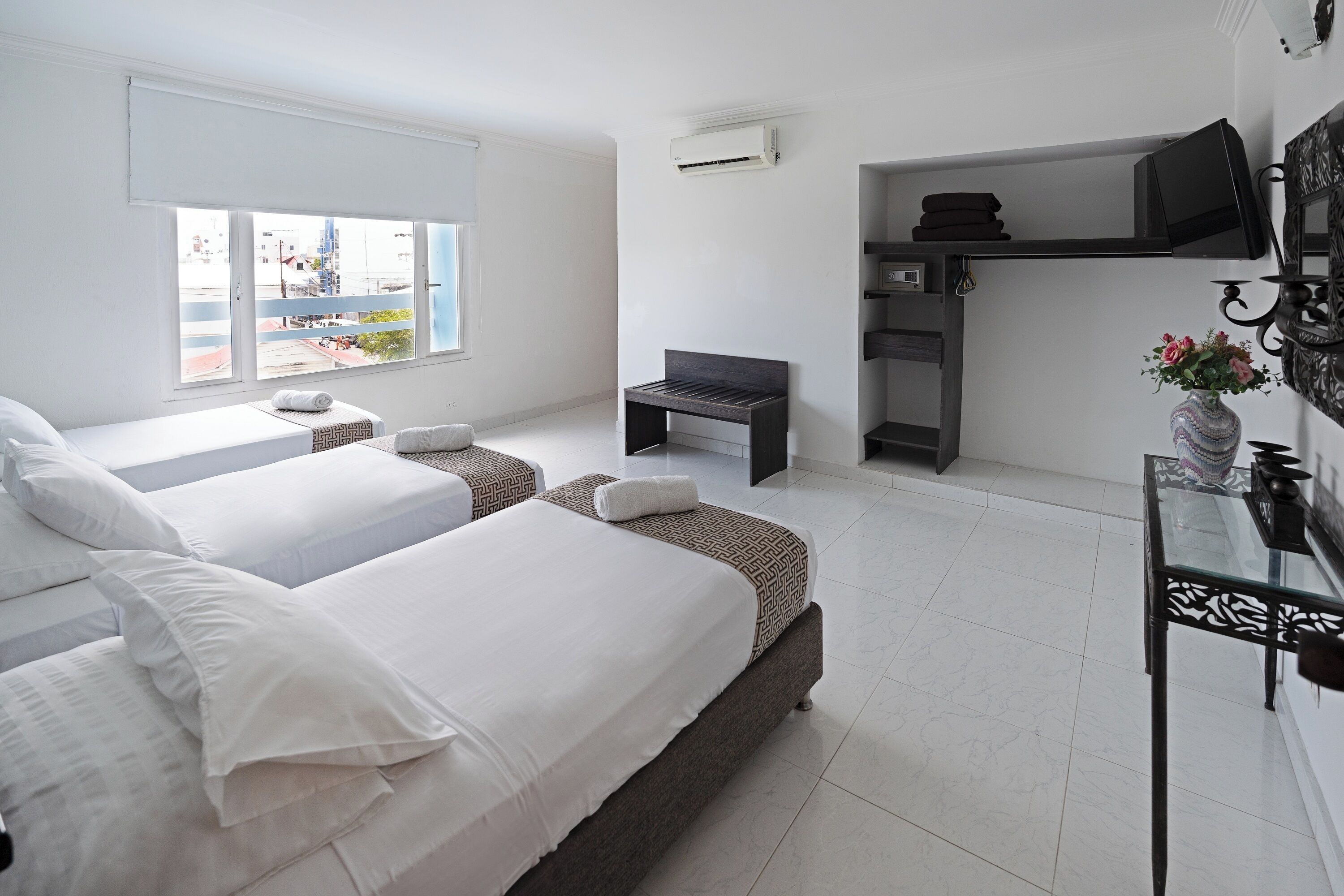 A modern hotel room with two beds, a small seating area, a TV, and a view of the city through the window.
