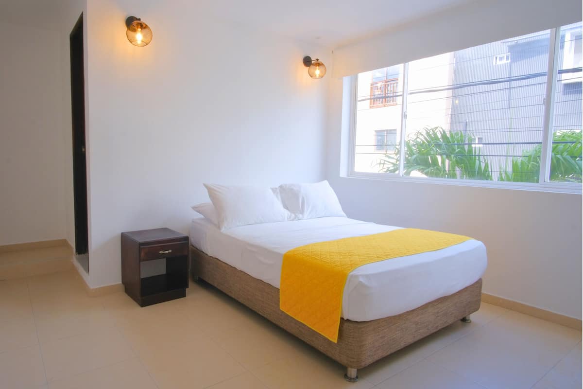 A bedroom with a bed, a nightstand, a window, and wall-mounted lights.