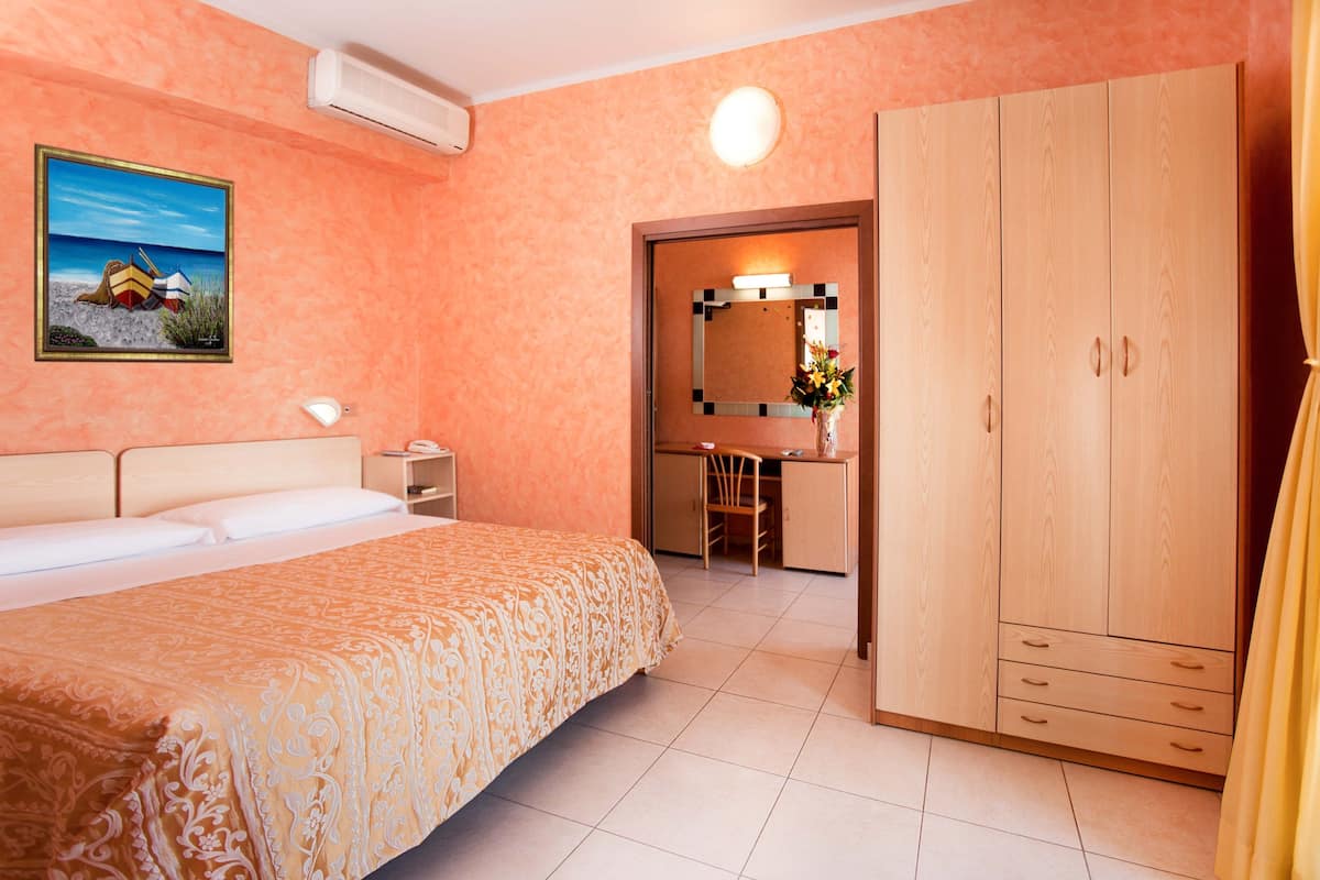 A hotel room with a bed, a desk, a wardrobe, and a bathroom visible through an open door.
