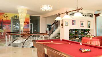A pool table in a well-lit room with a staircase, a chandelier, and framed pictures on the wall.