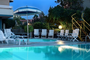 A swimming pool with lounge chairs and umbrellas, surrounded by greenery and a staircase. - Hotel Caesar (Cesenatico)