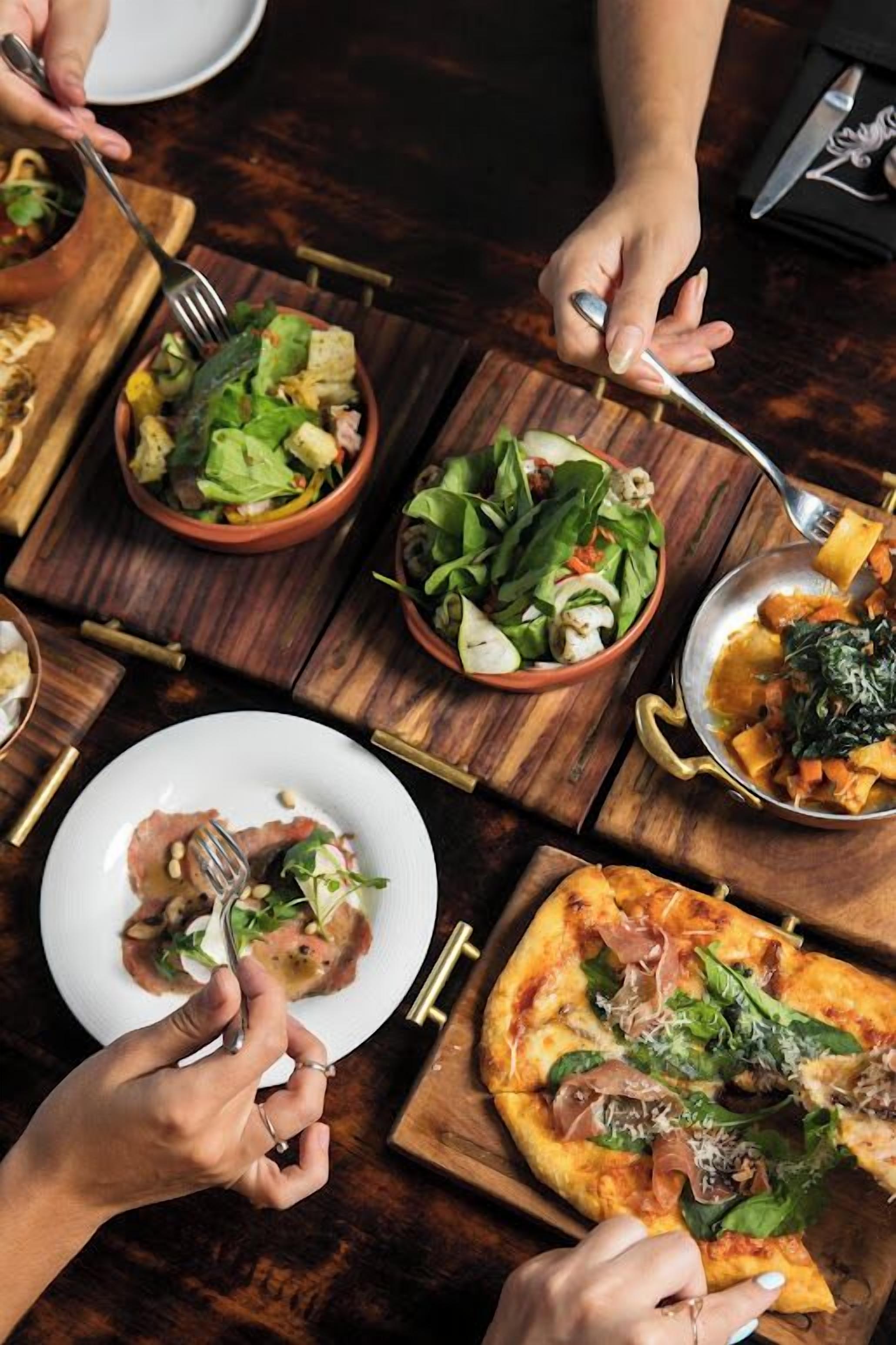 Een eettafel met diverse gerechten, waaronder salades en pizza's, die worden geserveerd.