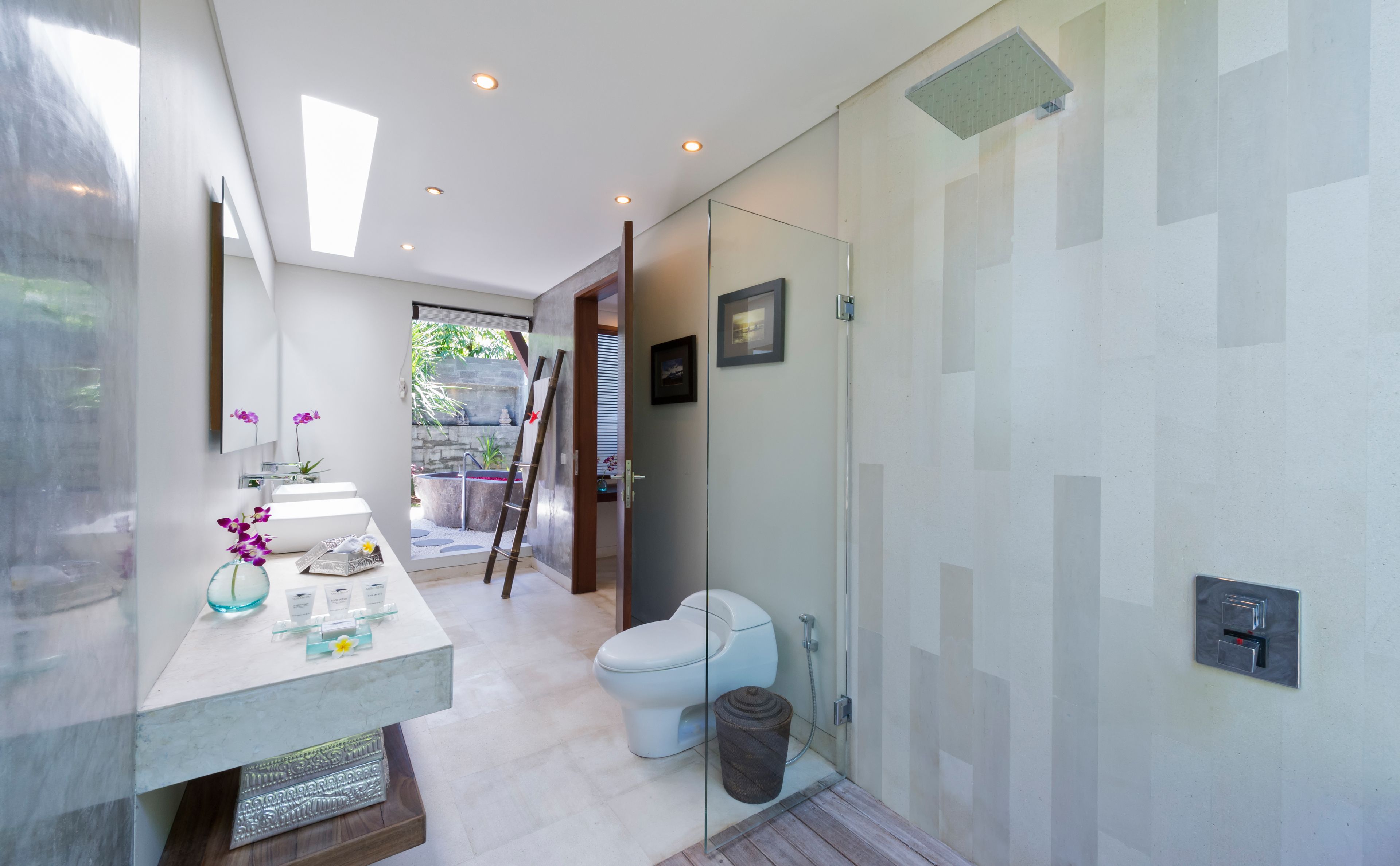 A modern bathroom with a glass shower enclosure, a white toilet, and a vanity with a mirror and a vase of flowers.