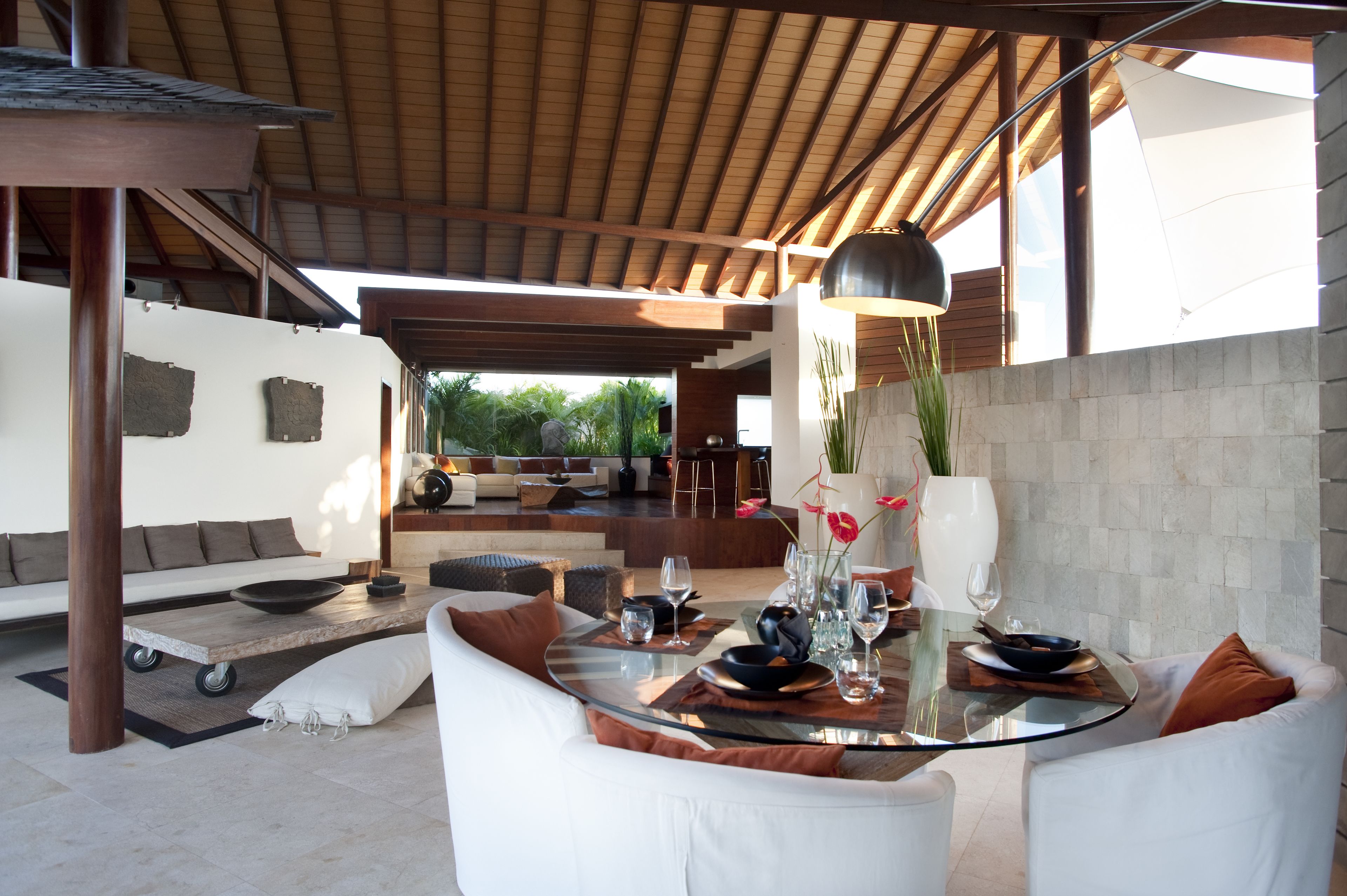 An outdoor dining area with a glass table, white sofas, and a stone wall.