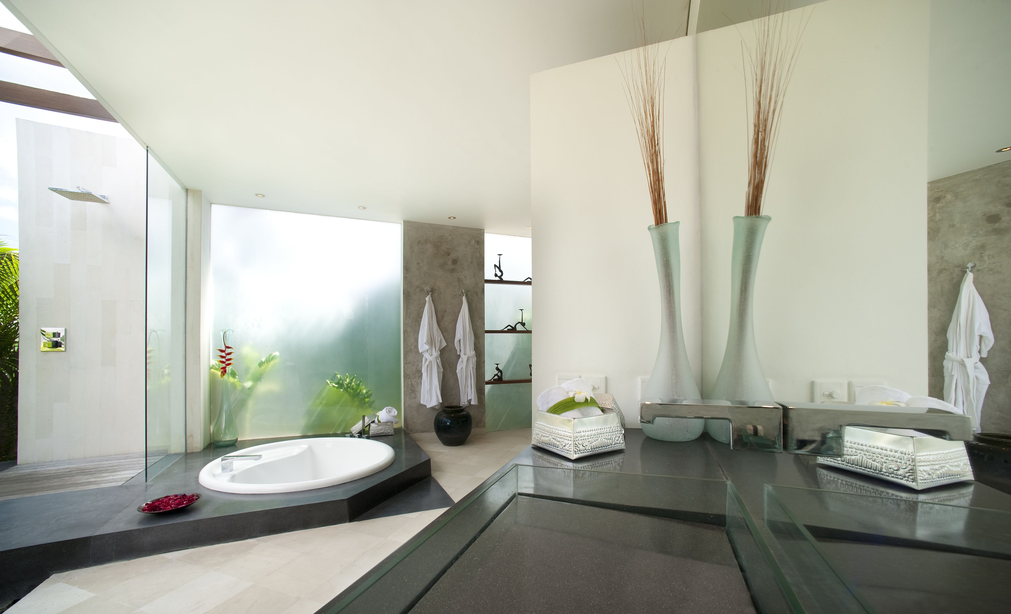 A modern bathroom with a large bathtub, two tall vases, and a glass shower enclosure.