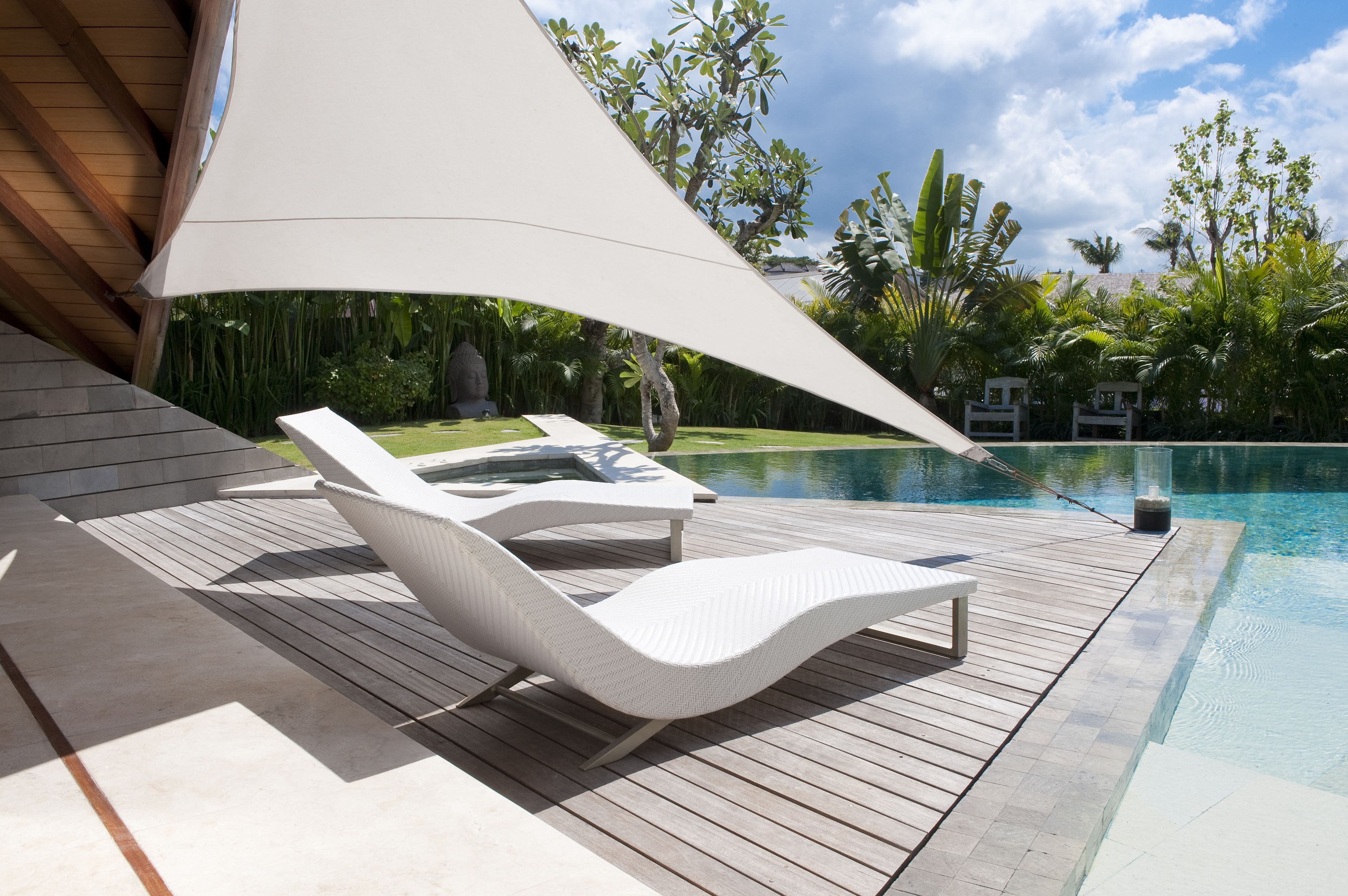 Une terrasse en bois avec des chaises longues blanches et une piscine.