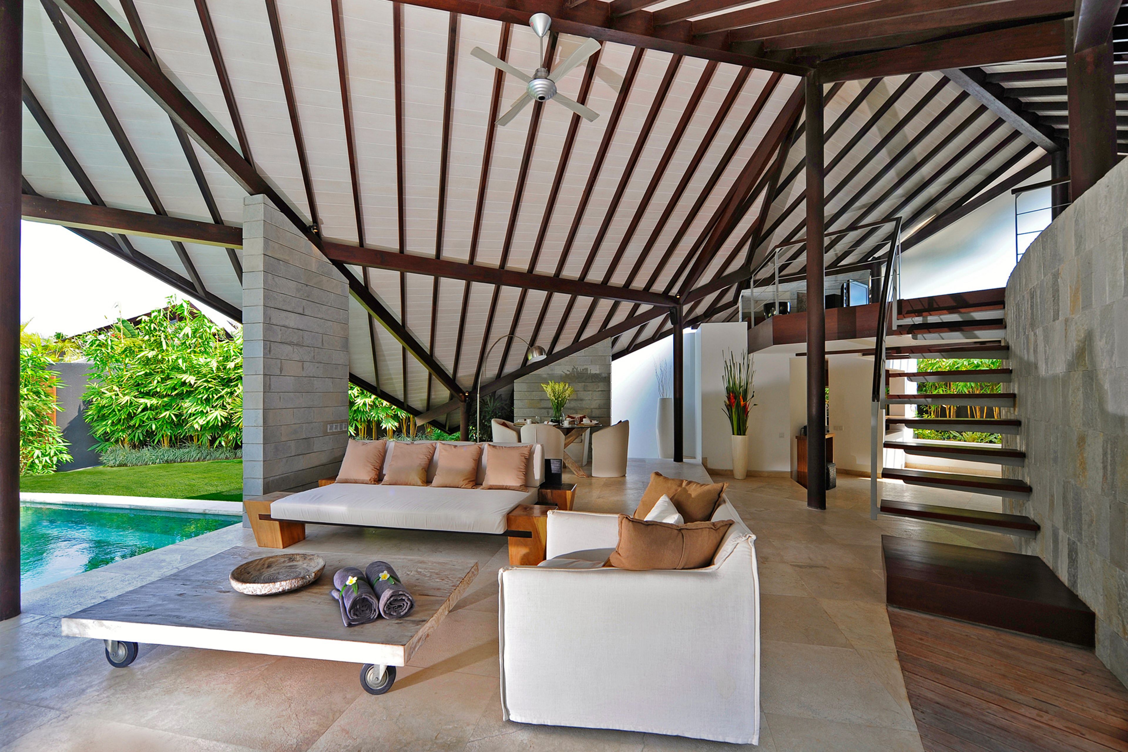 A modern outdoor living area with a pool, a sofa, a coffee table, and a staircase leading to an upper level.