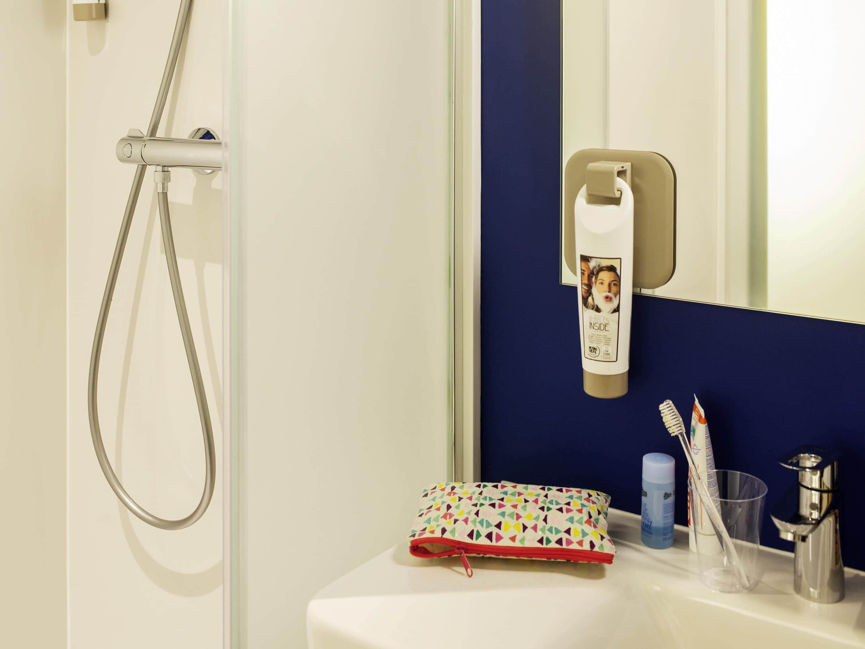 A bathroom with a shower, a mirror, a sink, and toiletries.