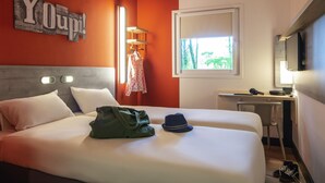 Une chambre d’hôtel avec un lit, un bureau, une télévision et une fenêtre donnant sur des arbres.