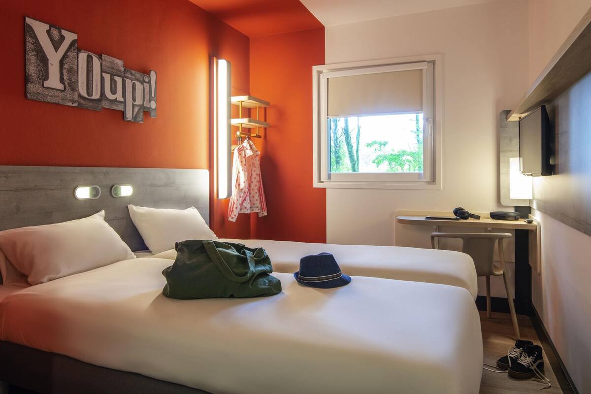 Een hotelkamer met een bed, een bureau, een televisie en een raam met uitzicht op bomen.