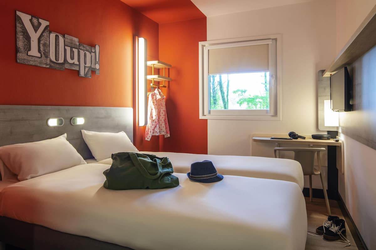 Ett hotellrum med en säng, ett skrivbord, en tv och ett fönster med utsikt över träd.