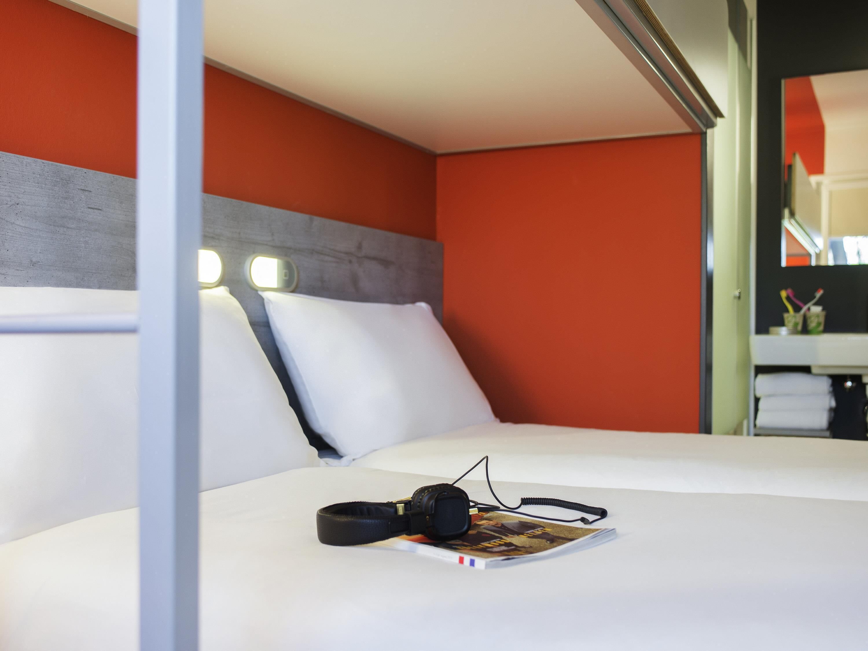 Una habitación de hotel con cama, almohadas, una revista y auriculares.