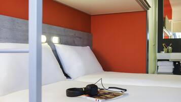 Una habitación de hotel con cama, almohadas, una revista y auriculares.