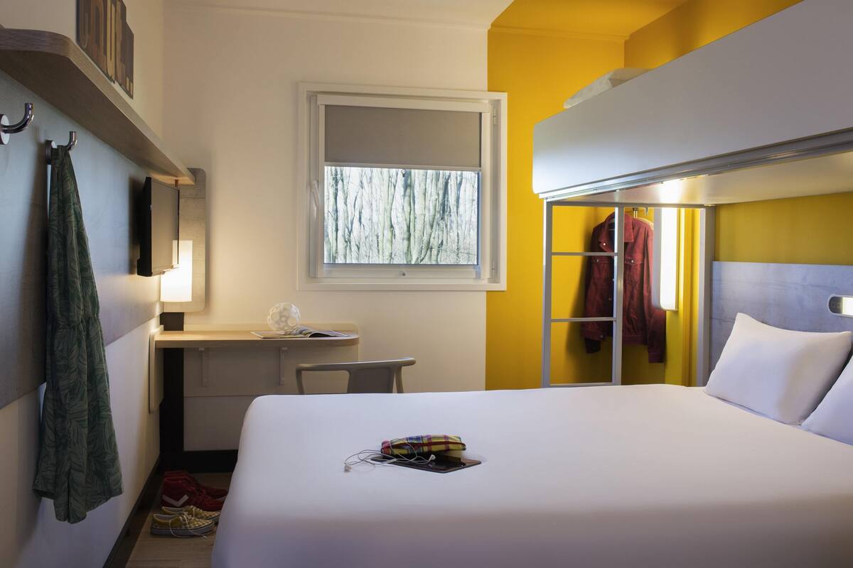 Ein Hotelzimmer mit Bett, Schreibtisch, Fenster und Kleiderhaken.