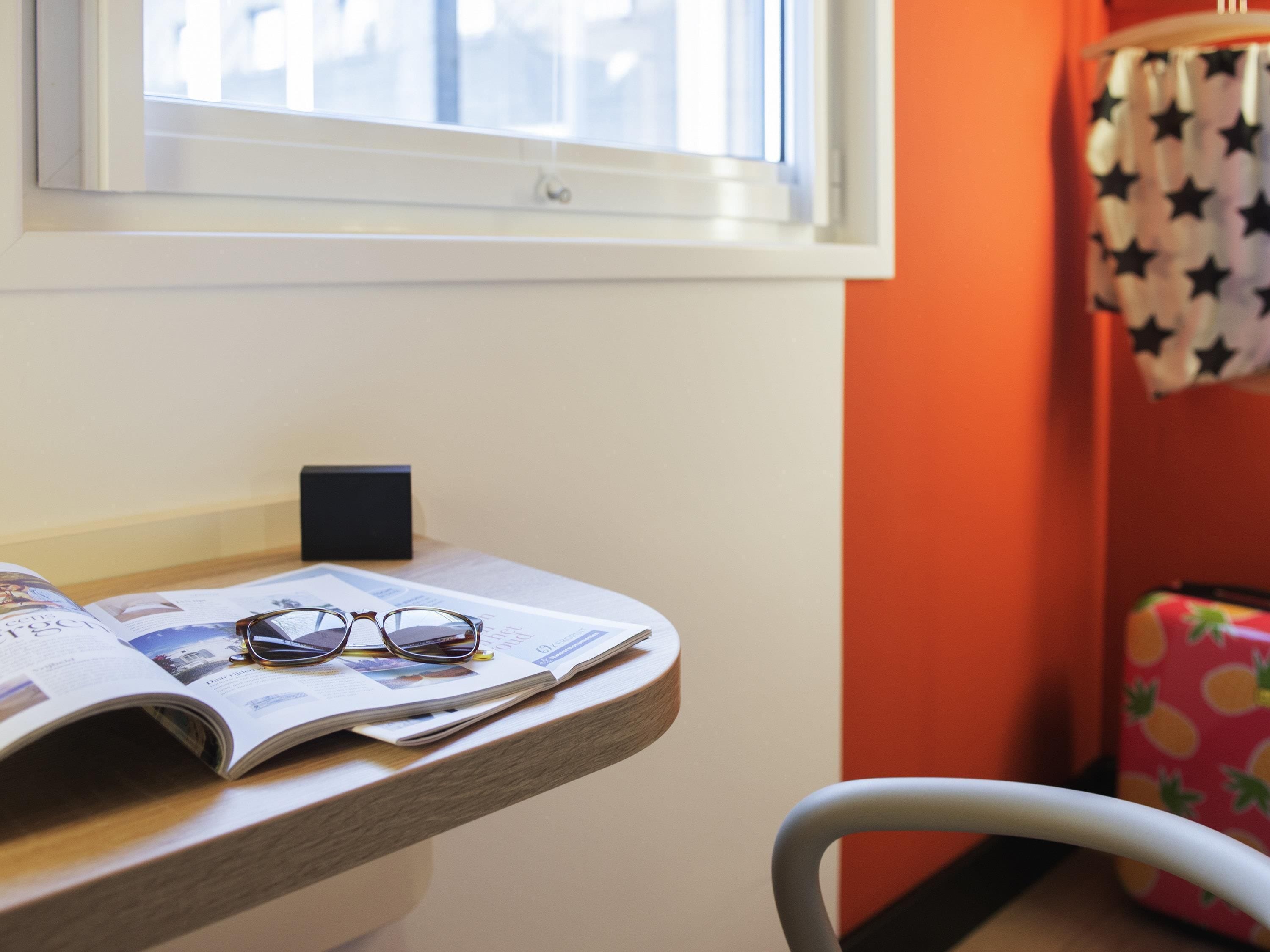 A room with a window, a table with a newspaper, glasses, and a black object.