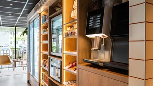 L’intérieur d’un café moderne, avec une machine à café, des étagères remplies de collations et une vue sur la rue.